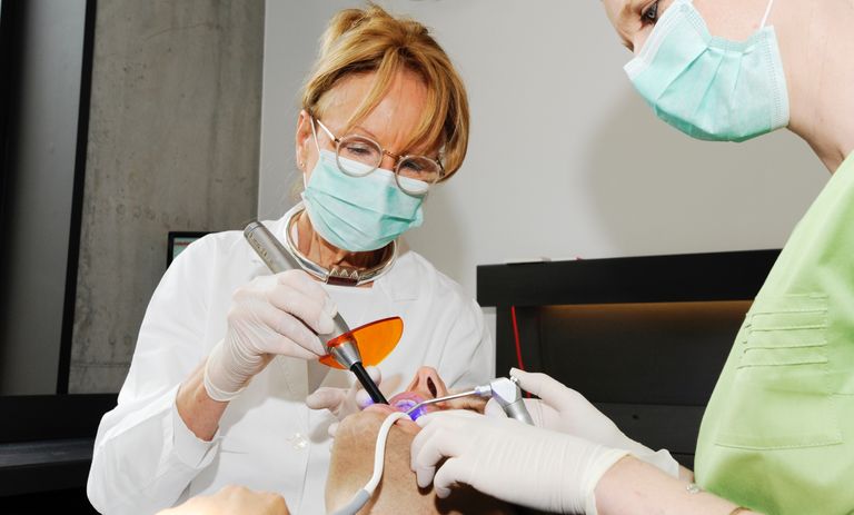 Orthodontist en mondhygiënist werken samen in de mond van een patiënt.